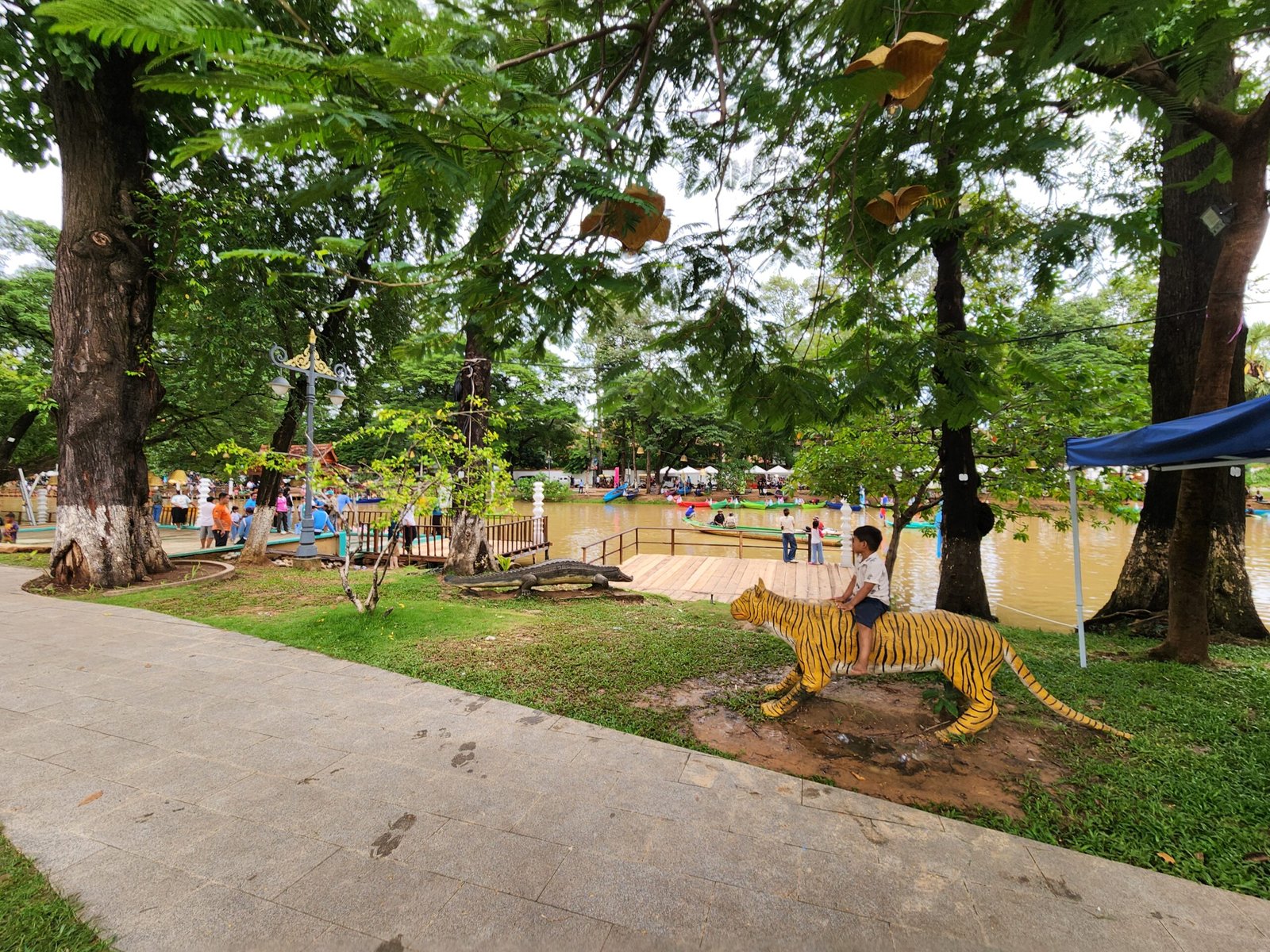 A boy rides the tiger statue as boats gather on the river