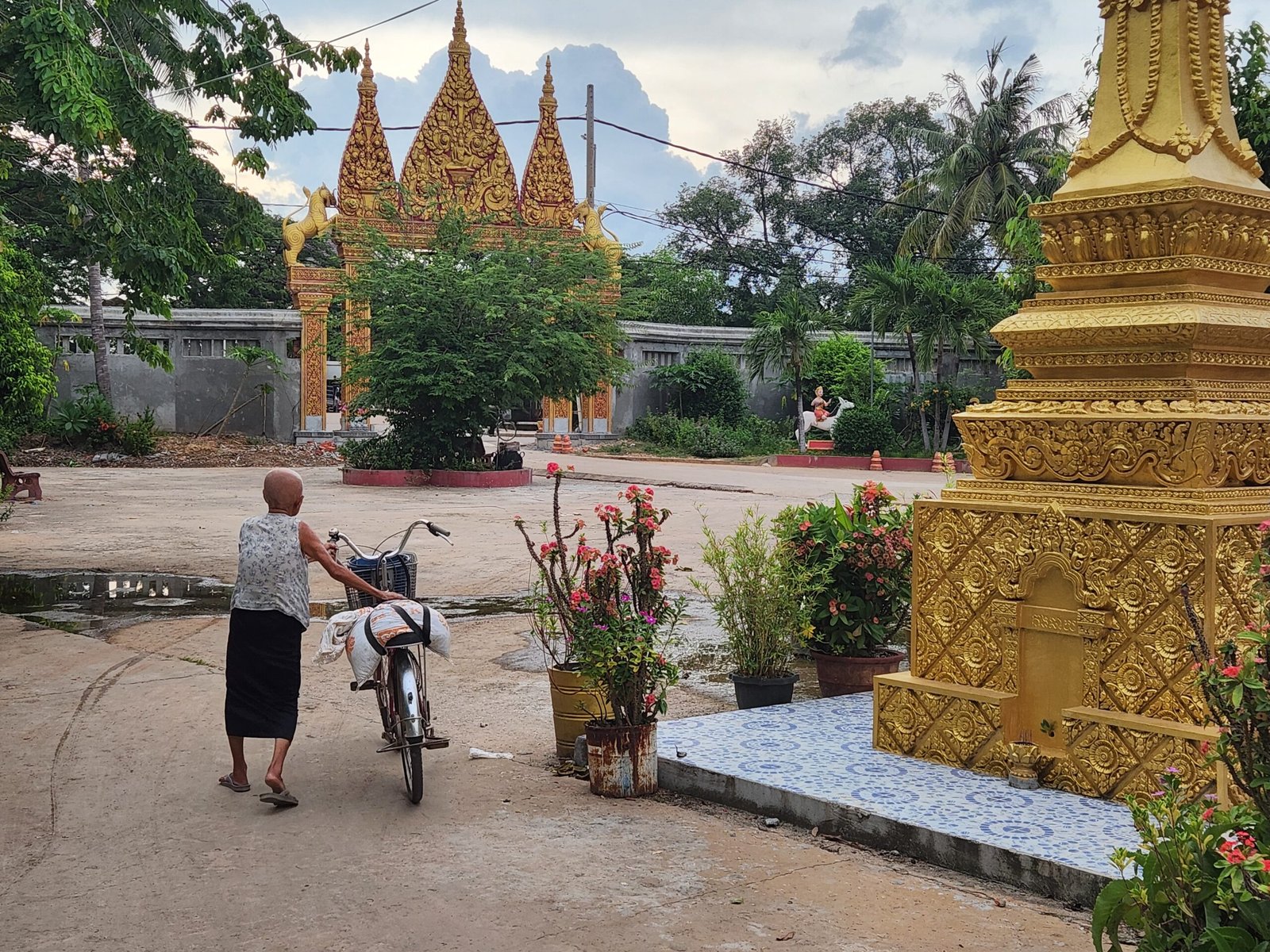 An elderly woman with her bicycle heads toward the golden gate entrance