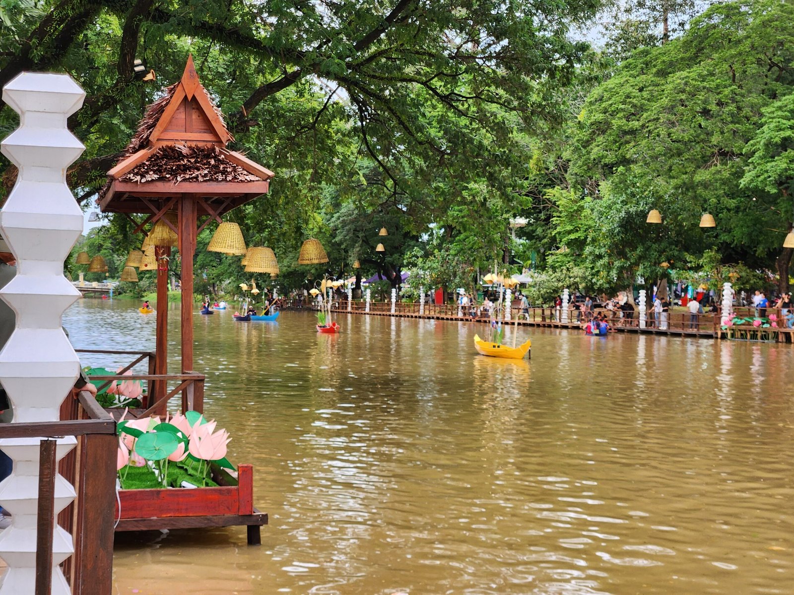 Hanging lanterns frame the lotus boat and a yellow canoe on the river