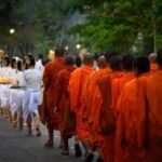 Buddhist monks in saffron robes processing at dusk past candle-bearing dancers during the annual monk blessing at Jaya House River Park, Siem Reap